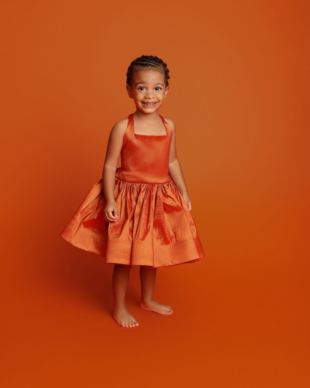 Young girl smiling in an orange satin halter dress, posed against a matching orange background in Covington, GA