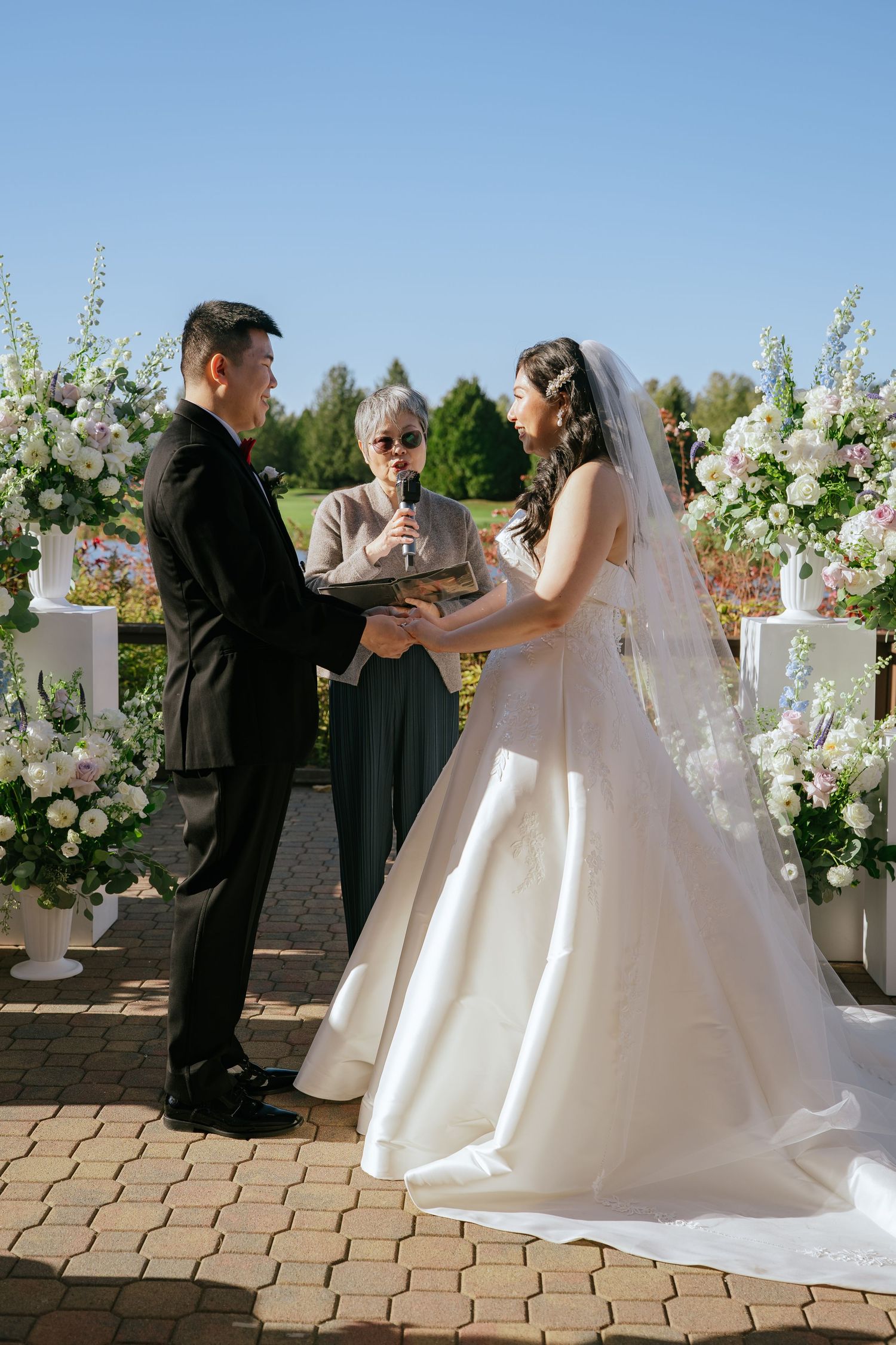 Jennifer and Riley holding hands at the altar with their officiant during their outdoor ceremony at Riverway Clubhouse in Burnaby