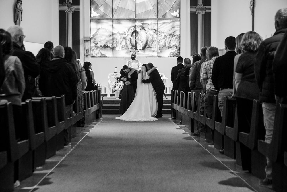 Black and white photo of a bride and groom embracing at the altar during a church wedding ceremony as guests watch from the pews.