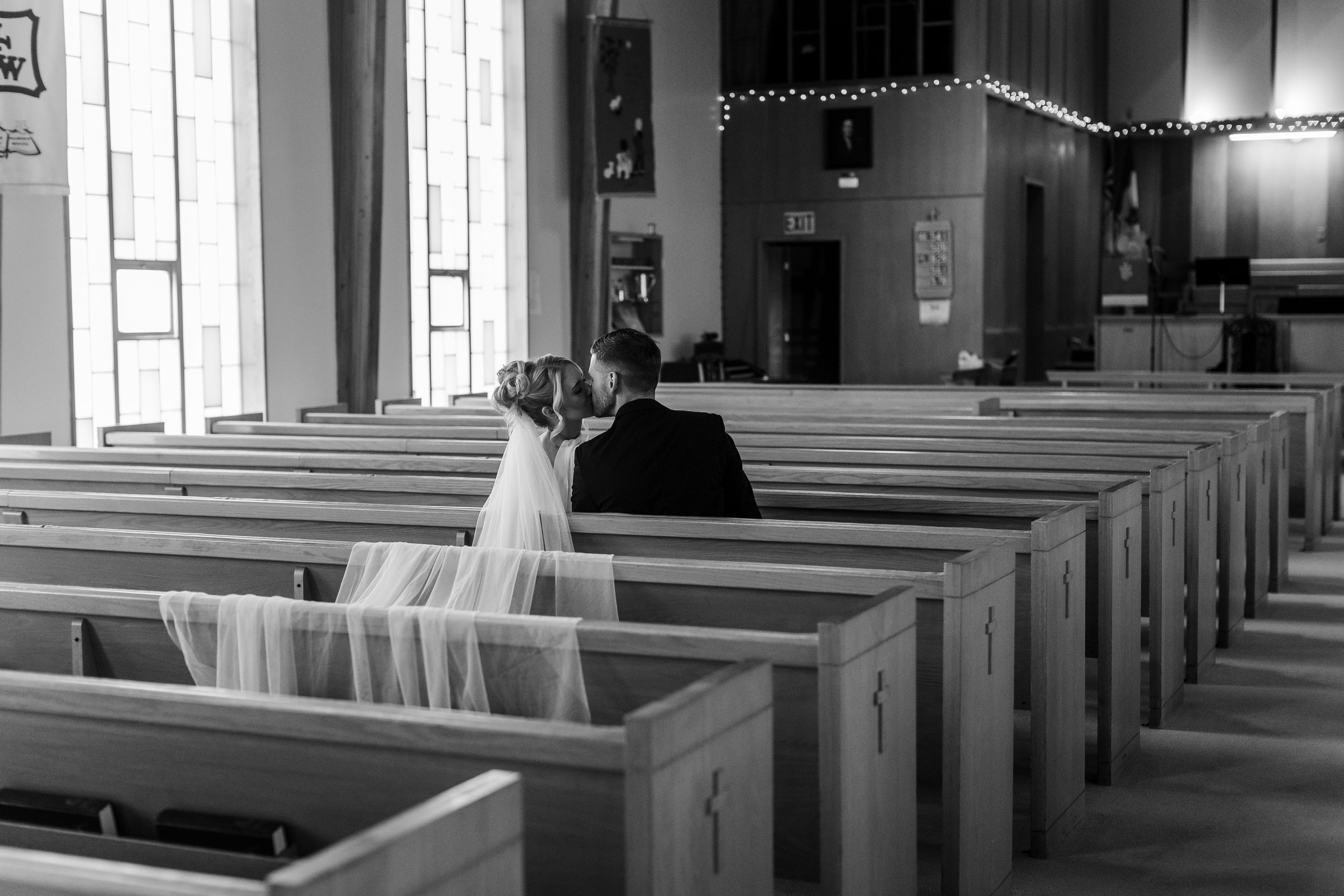 Black and white photo of a bride and groom sitting together in church pews on their wedding day.