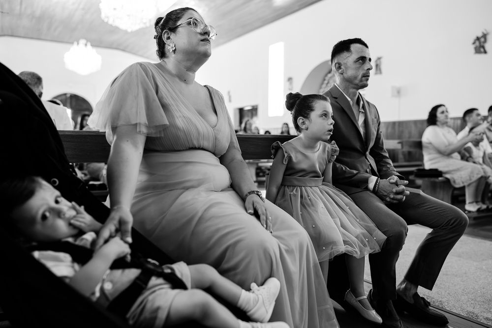 Black and white photo of a family seated in church pews during a wedding ceremony, including a woman, man, and young girl in formal attire.