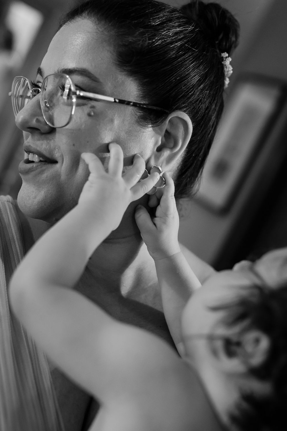 Black and white photo of a woman with glasses as a baby touches her ear near an earring.