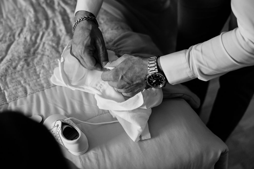 Black and white photo of elderly hands folding white fabric, with a watch and bracelet visible on wrists.