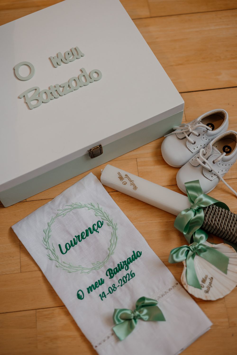 Personalized baptism keepsake box with embroidered cloth, baby shoes, and green ribbon decorations for Lourenco, dated 14-08-2026.