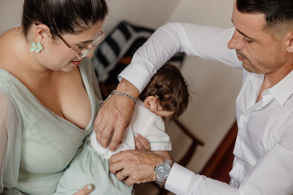 A couple tenderly caring for their newborn baby, with the mother in a sage green dress and father in a white shirt.