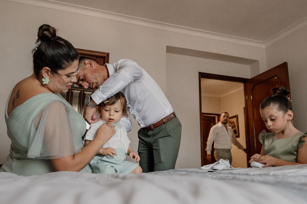 Family gathering in a bedroom with a woman holding a baby, a man leaning in, a young girl, and another person in background.