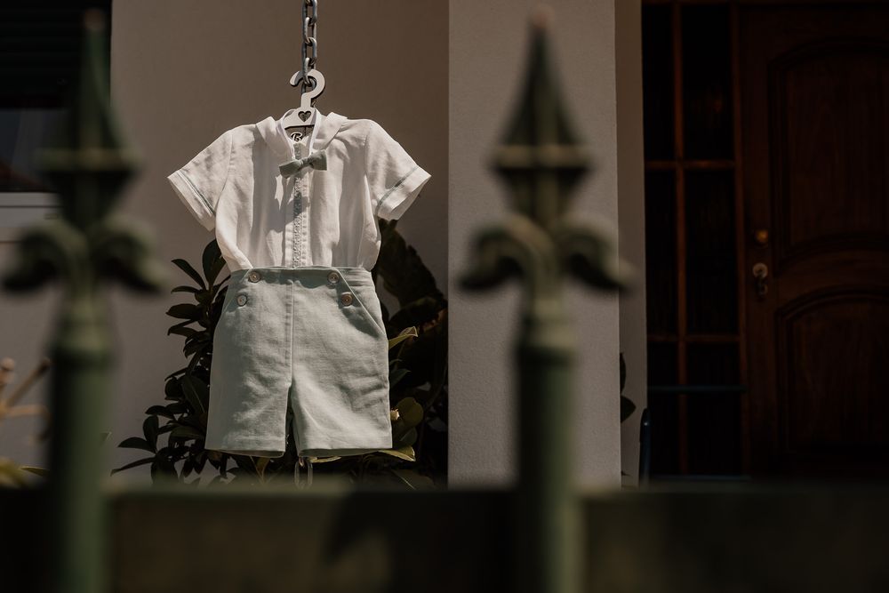 A white short-sleeve shirt and light green shorts hanging on a hanger outdoors near a fence.