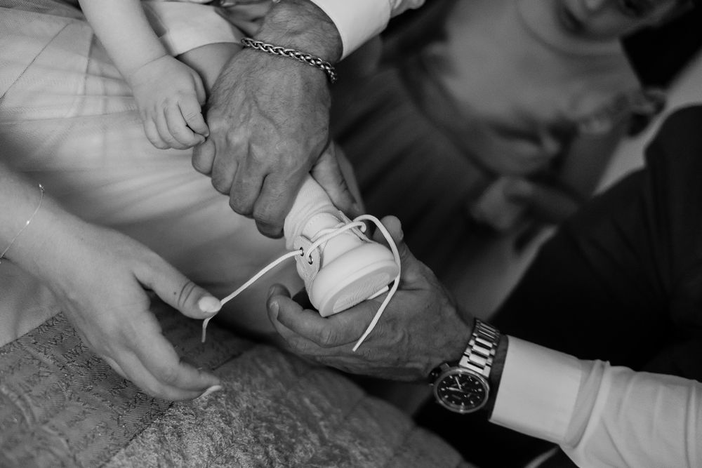 Elderly hands tying white shoelaces on a small child's shoe, black and white photo.
