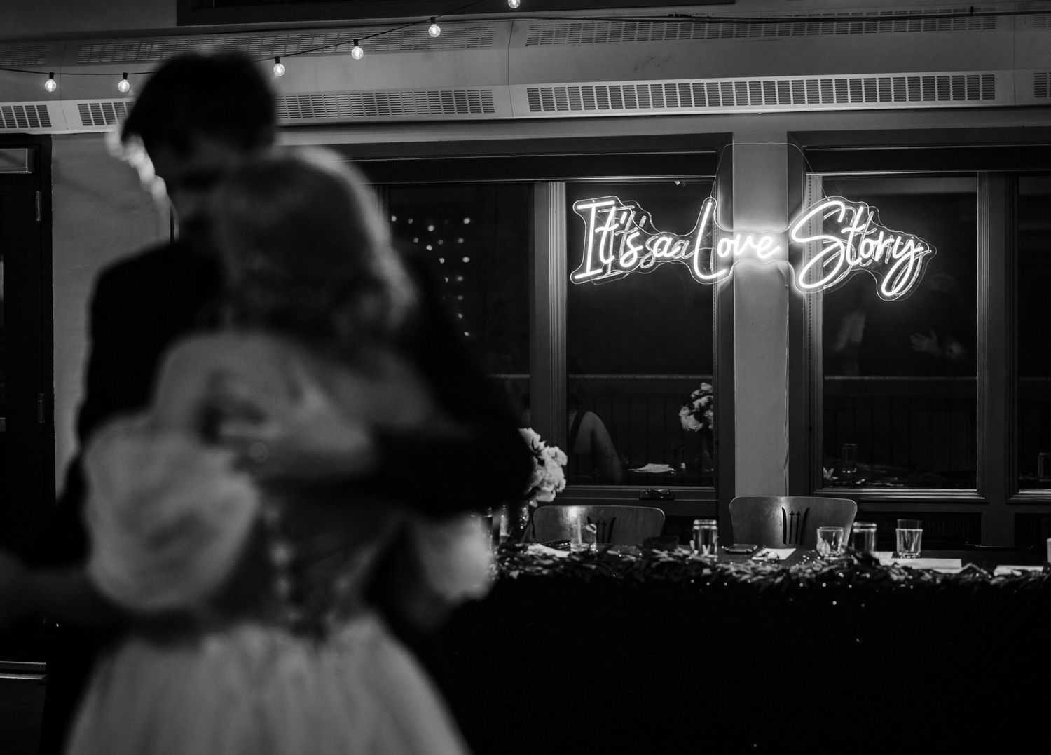 It's a Love Story neon sign glowing behind the couple's first dance in the Rundleview Room, Canmore