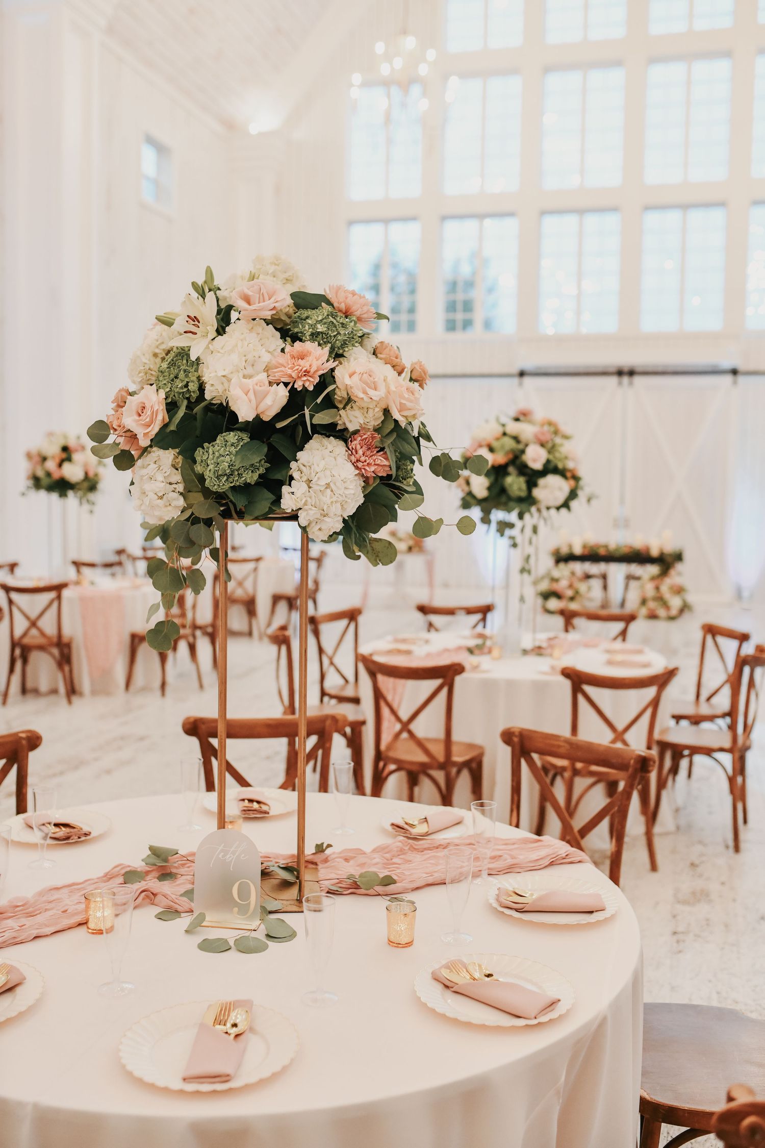 Elegant reception tables with white linens, mauve accents and tall floral centerpieces