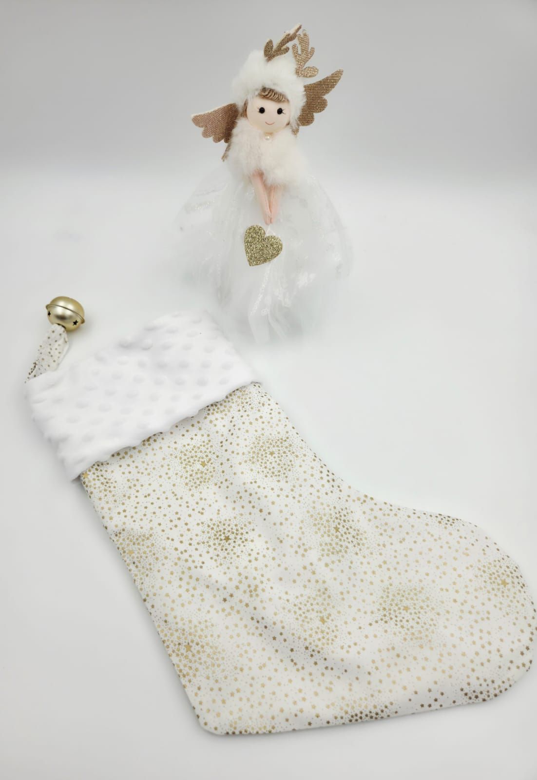 White and gold Christmas stocking with faux fur cuff beside a decorative angel ornament with glitter heart.