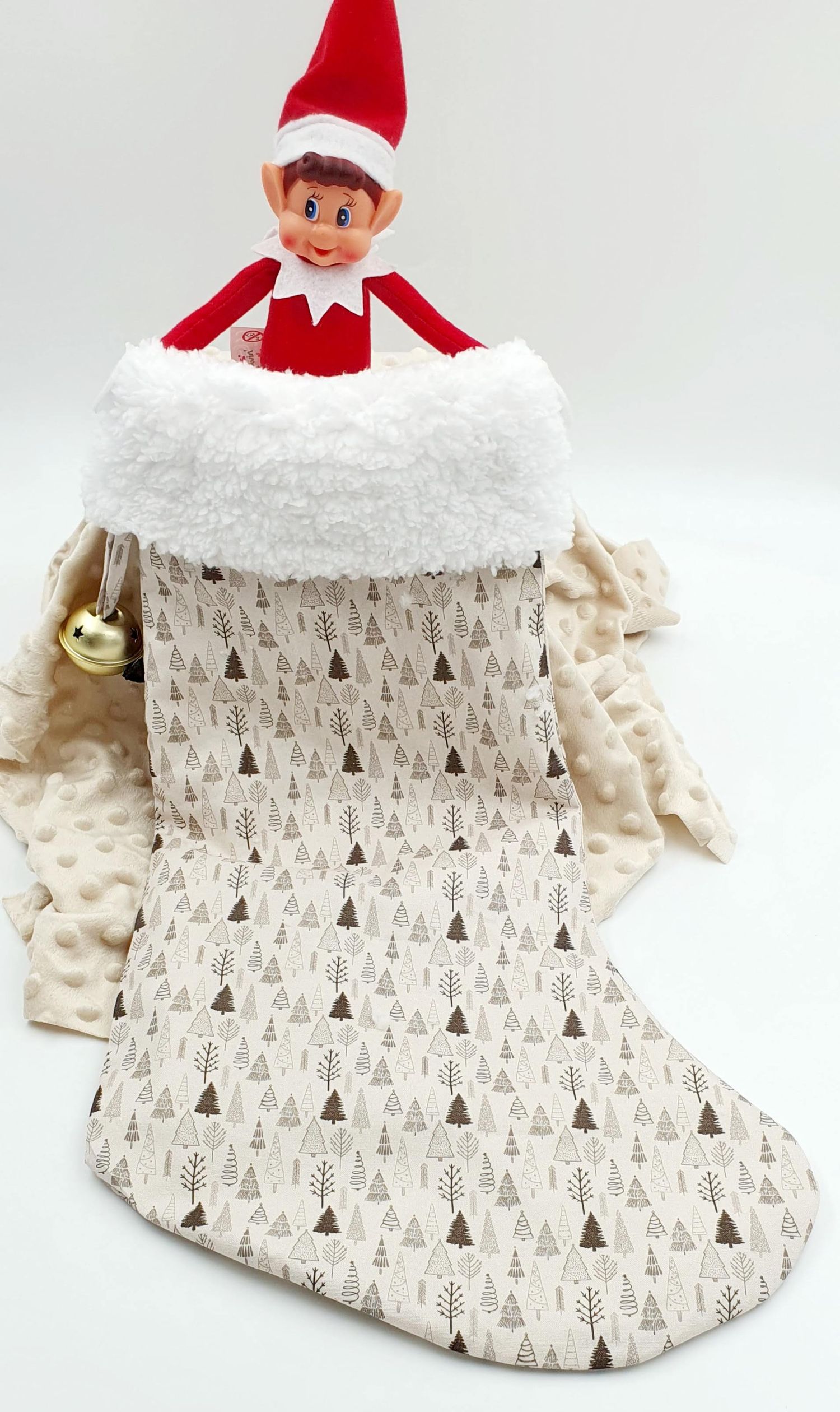 Elf on the Shelf doll sitting in a cream Christmas stocking with tree pattern and white faux fur trim.