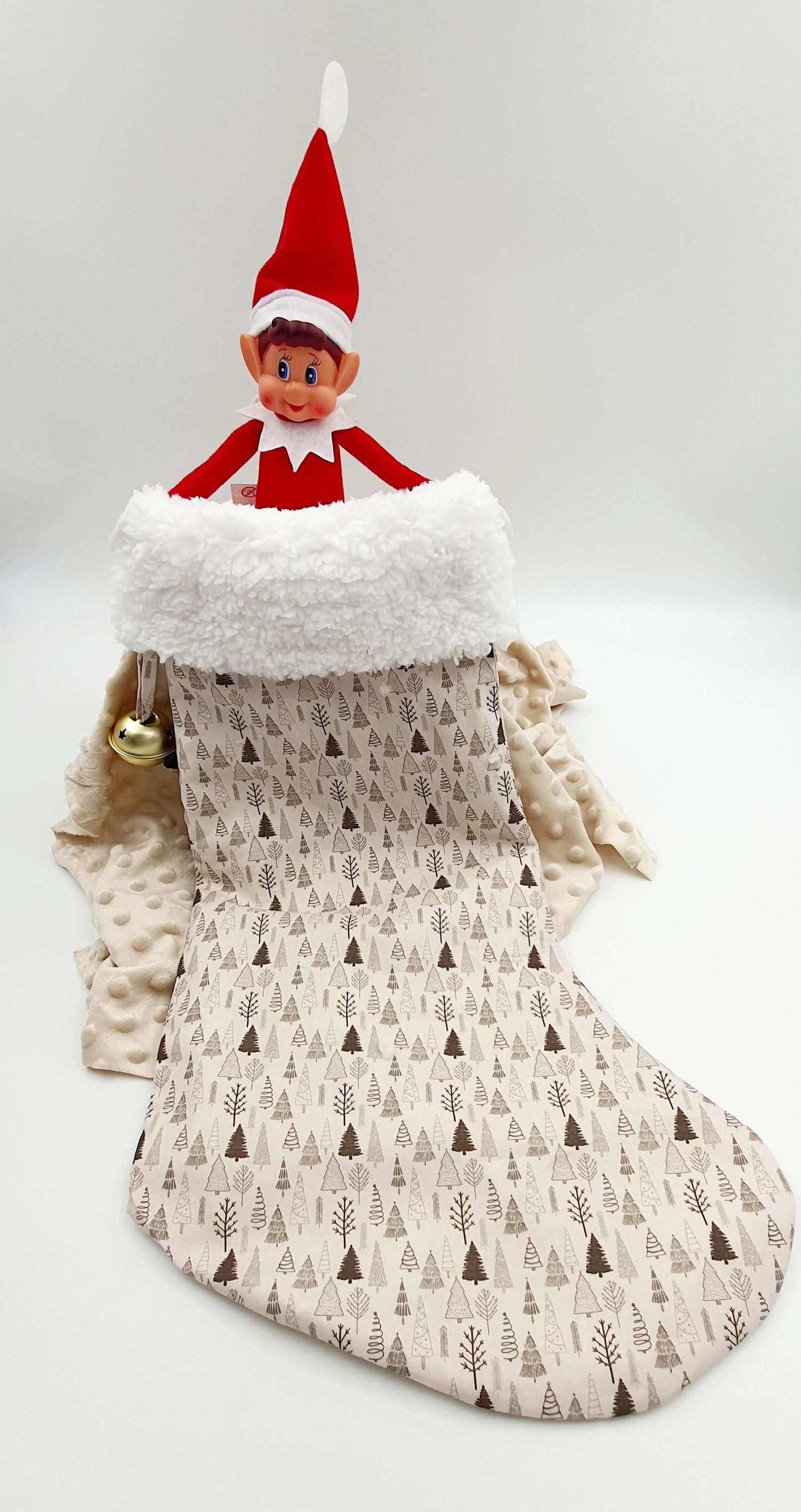 Elf on the Shelf doll peeking out of a cream Christmas stocking with festive tree pattern and white faux fur trim.