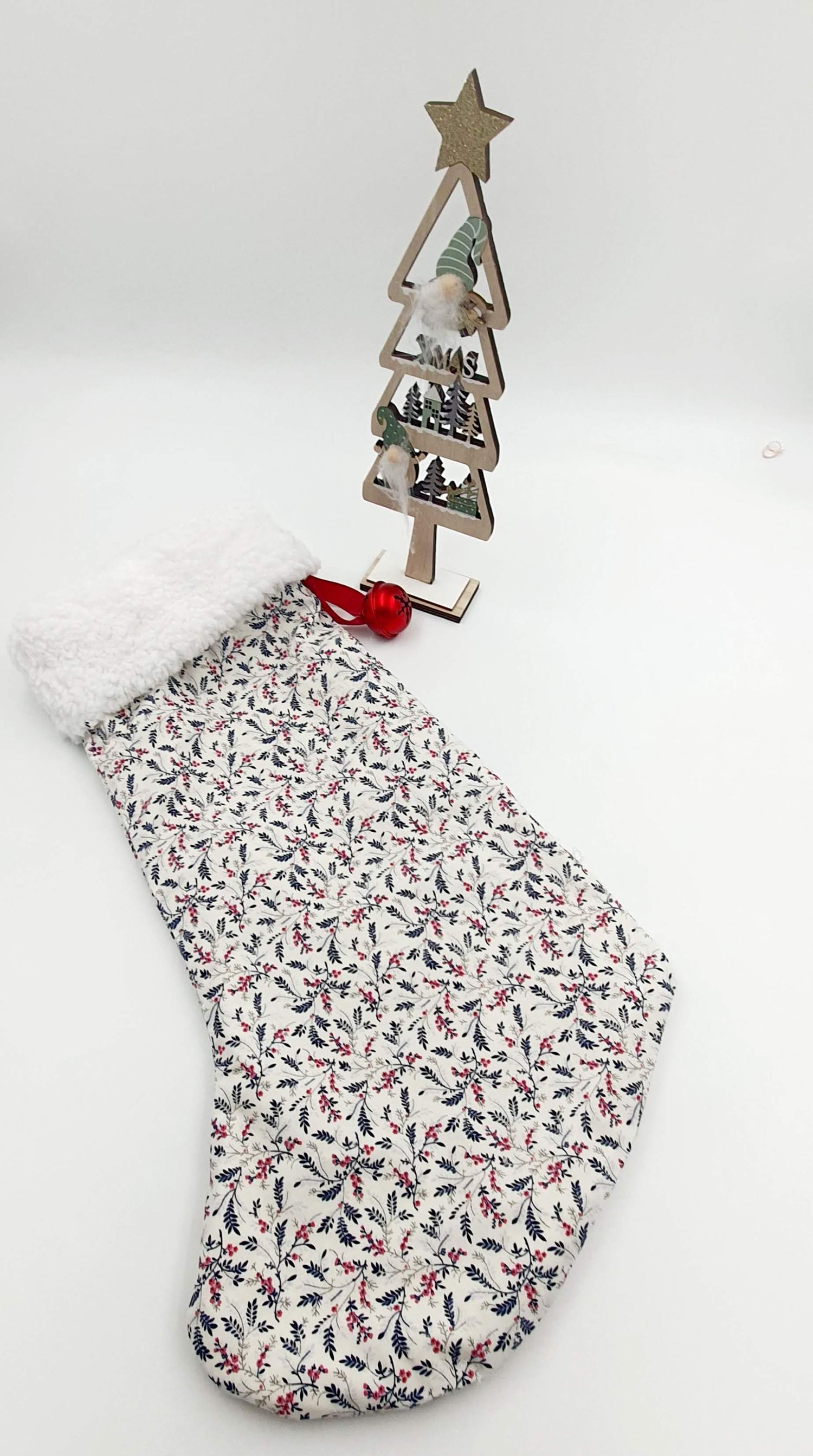 Christmas stocking with holly berry print and white fur trim beside a wooden decorative tree.