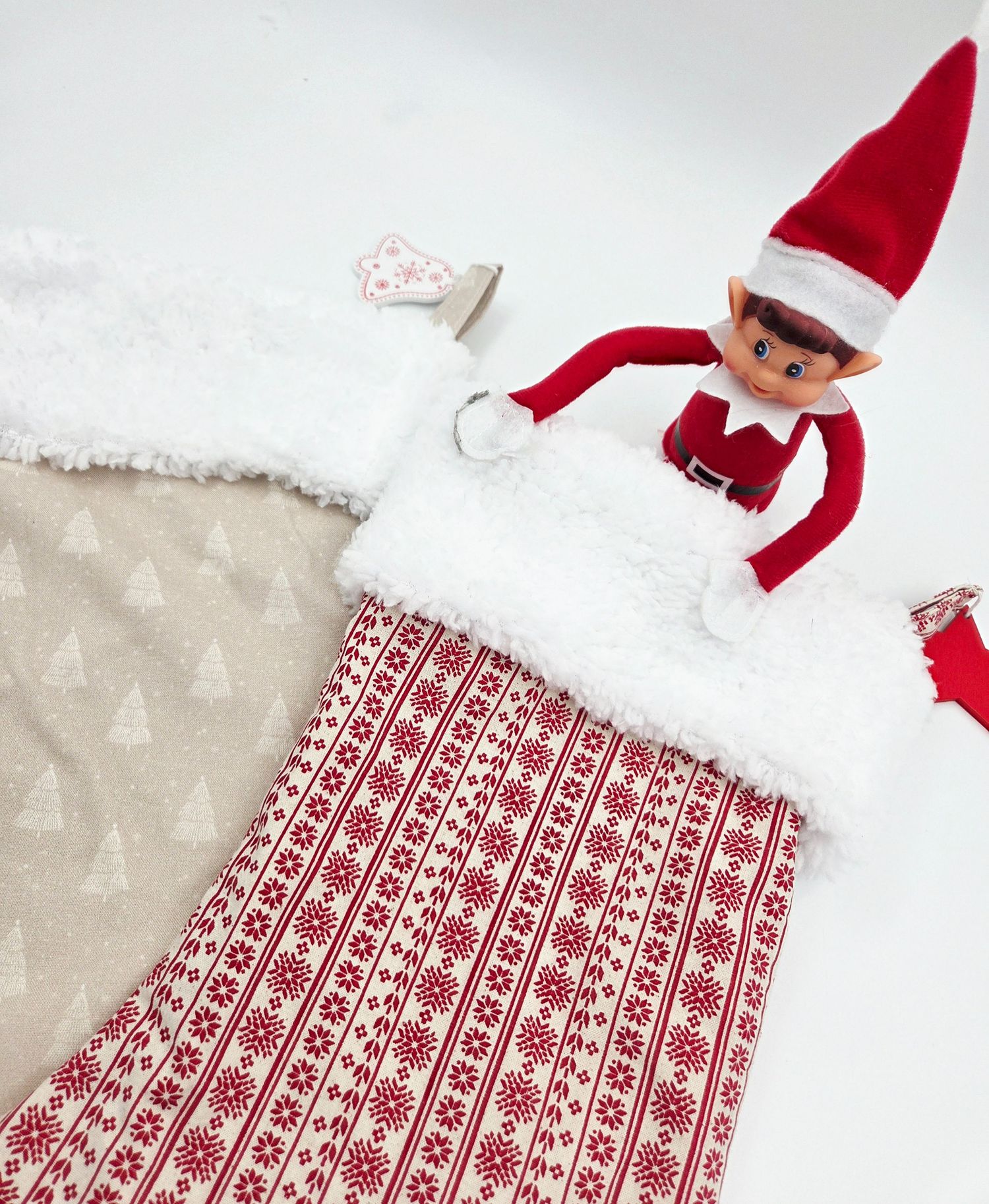 Elf on the Shelf doll peeking out of a red and white Nordic pattern Christmas stocking with white faux fur trim.