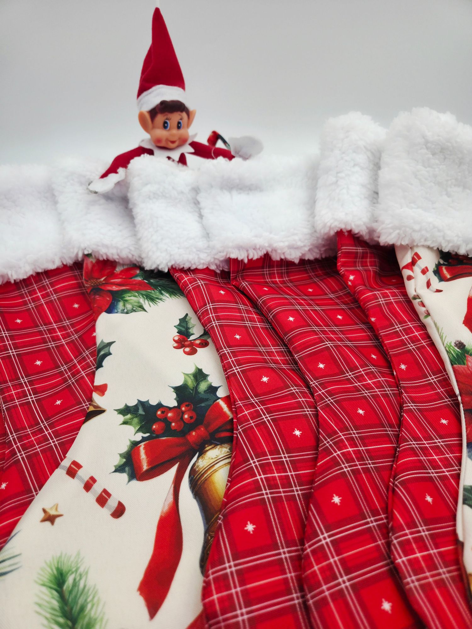 Elf on the Shelf doll peeking over red plaid and holiday-print Christmas stockings with white fluffy trim.