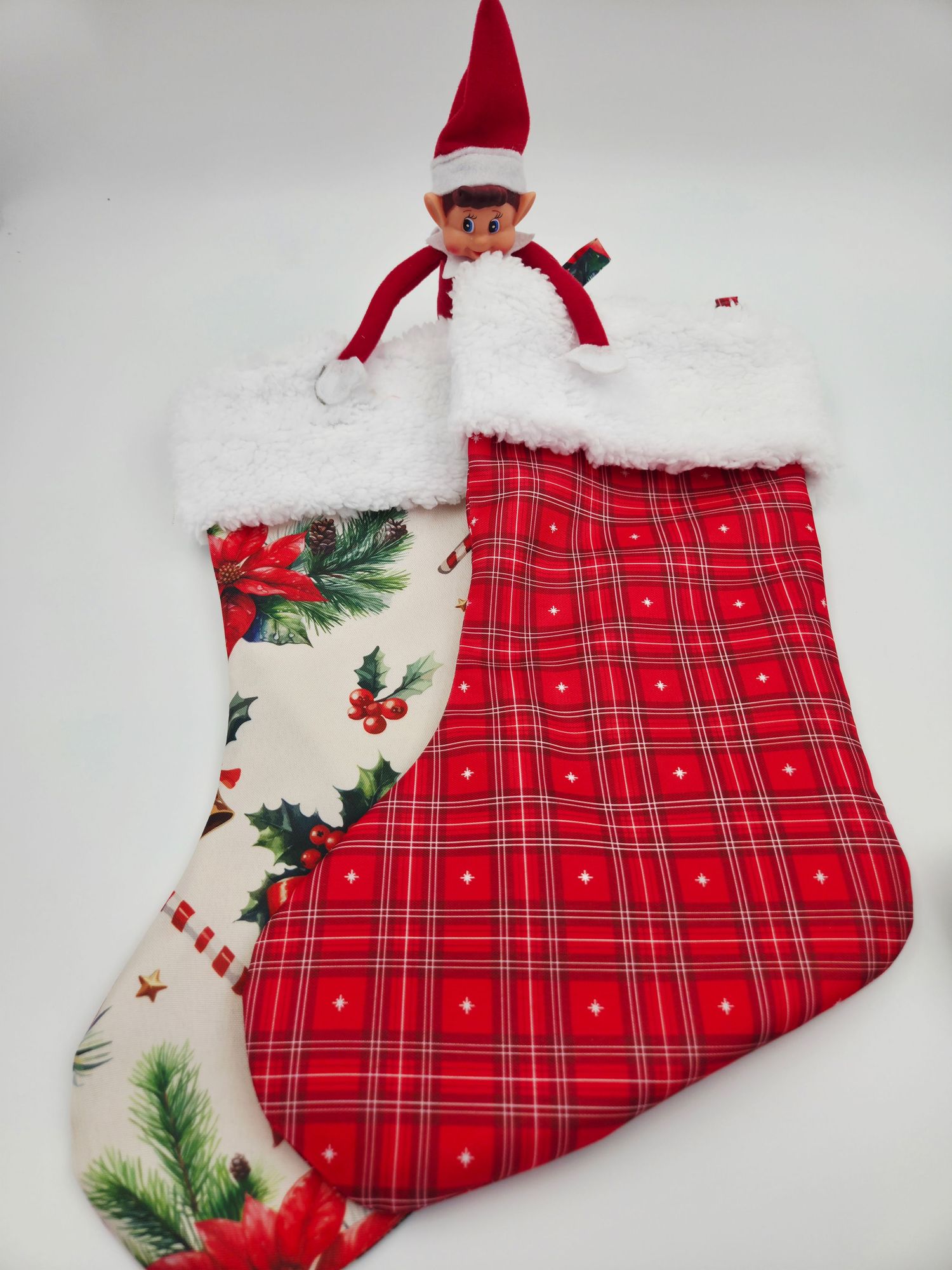 Red plaid Christmas stocking with holly print and white fur trim, featuring an Elf on the Shelf peeking out from the top.