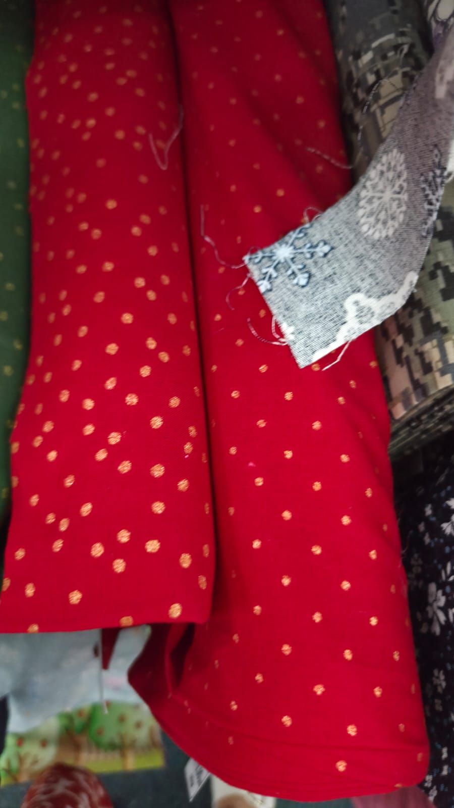 Red fabric with gold polka dots pattern, folded and displayed alongside other textile materials.