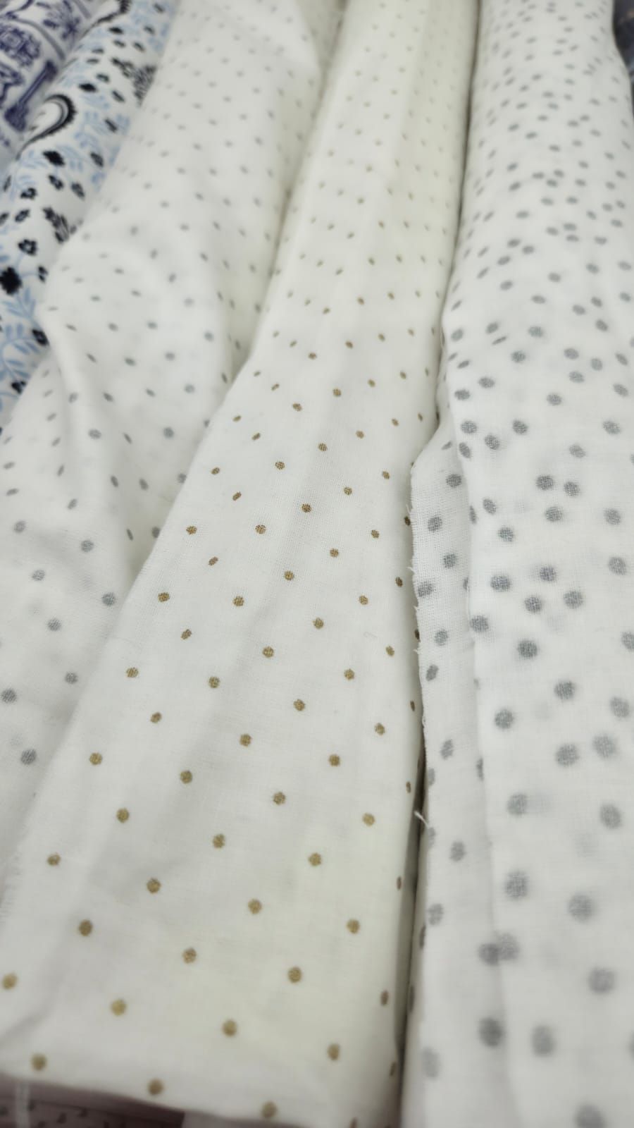 White fabric rolls with gold and silver polka dots pattern, ideal for quilting or crafting projects.