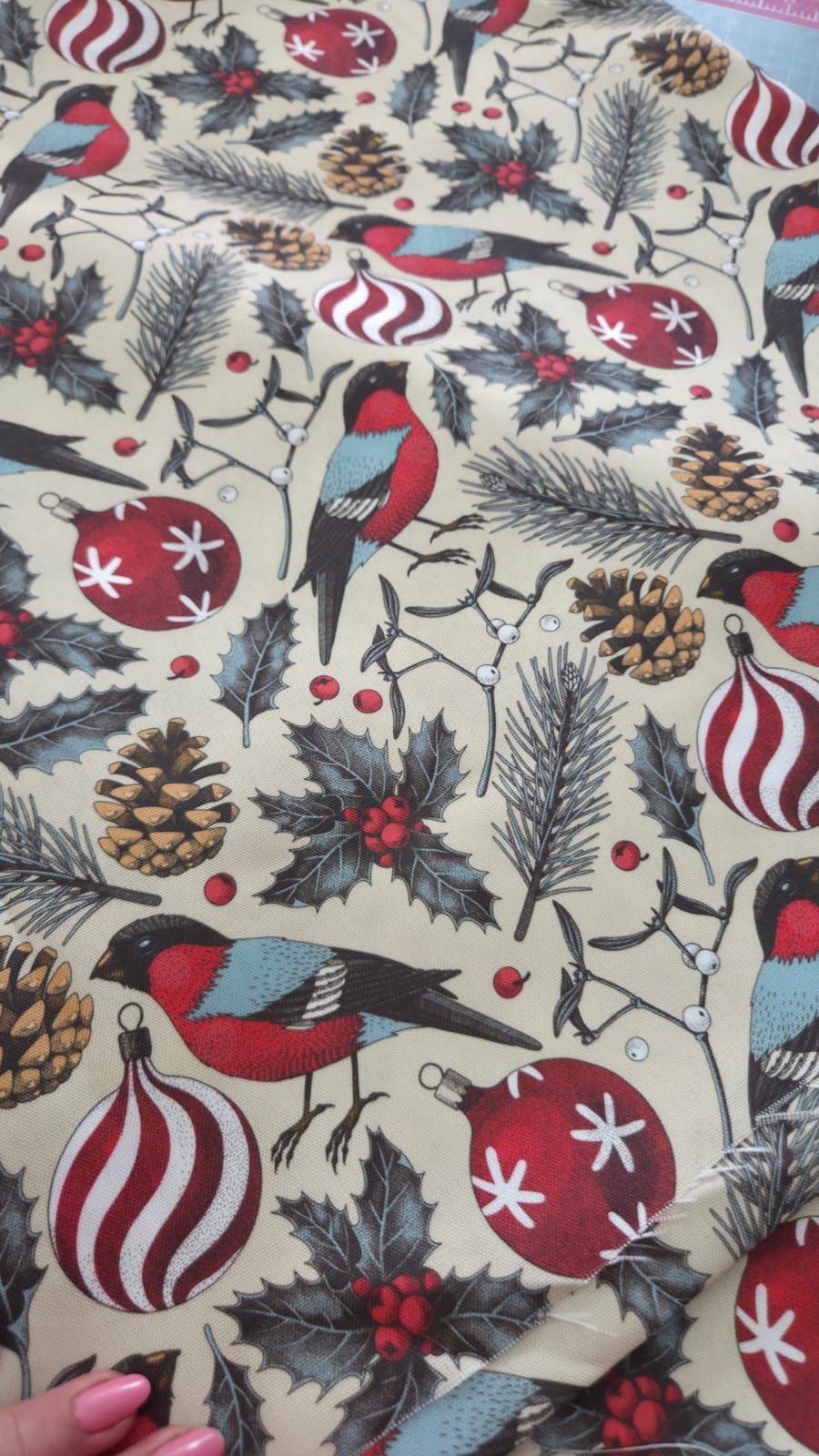Christmas wrapping paper featuring red birds, pine cones, holly, berries, and ornaments on a beige background.