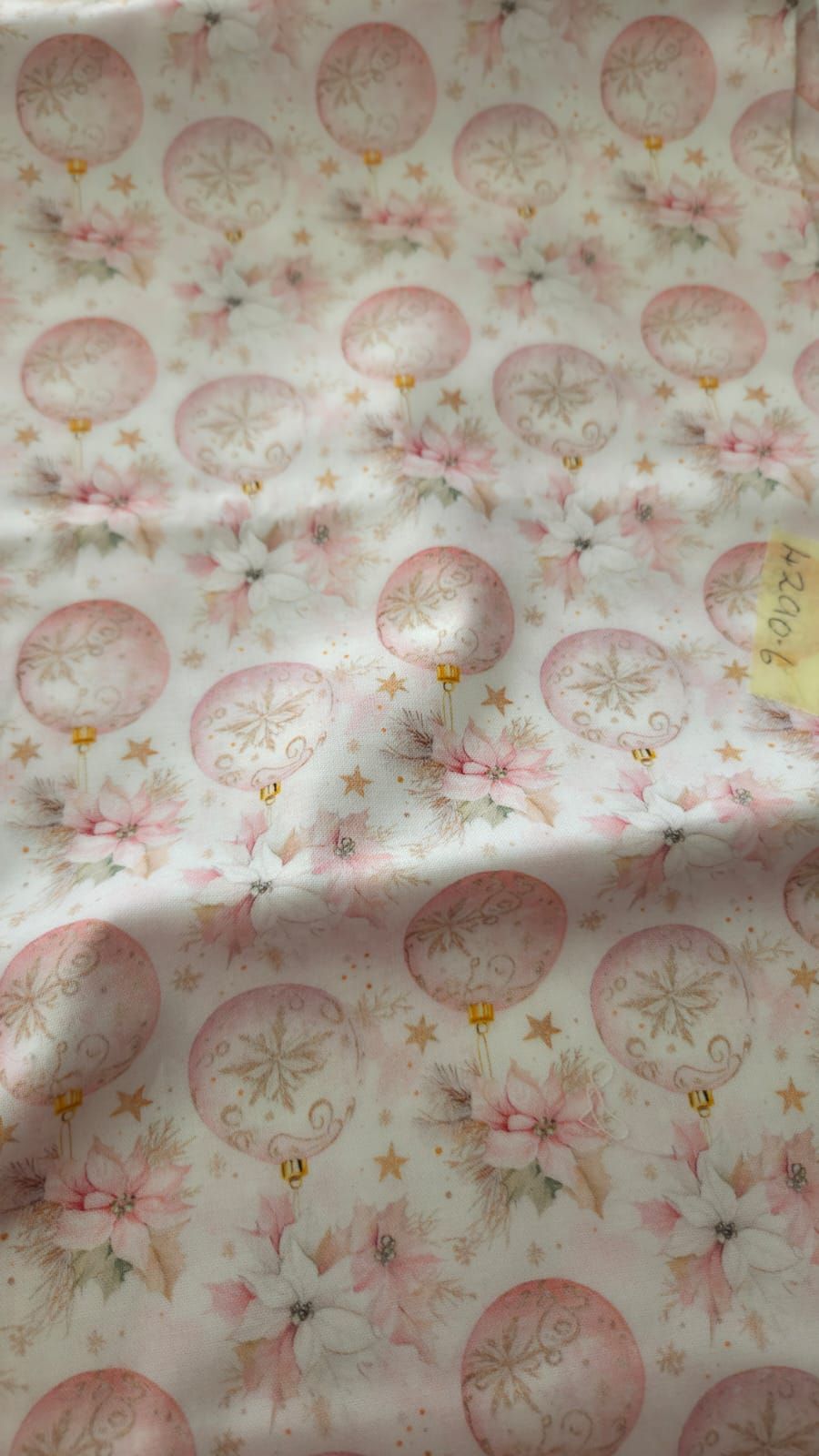 Pink Christmas fabric featuring ornaments, poinsettias, gold stars, and bells on a white background.