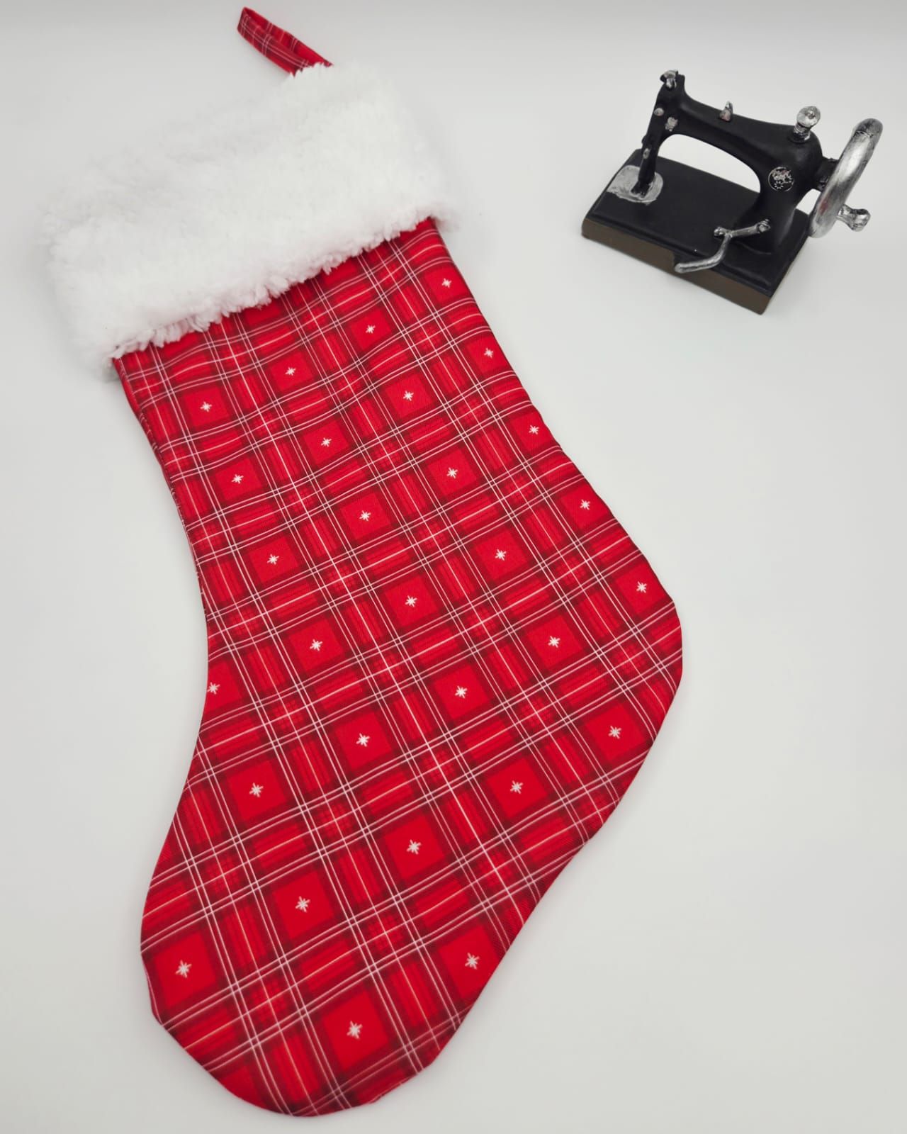 Red plaid Christmas stocking with white faux fur cuff, featuring star accents, displayed next to a miniature sewing machine.