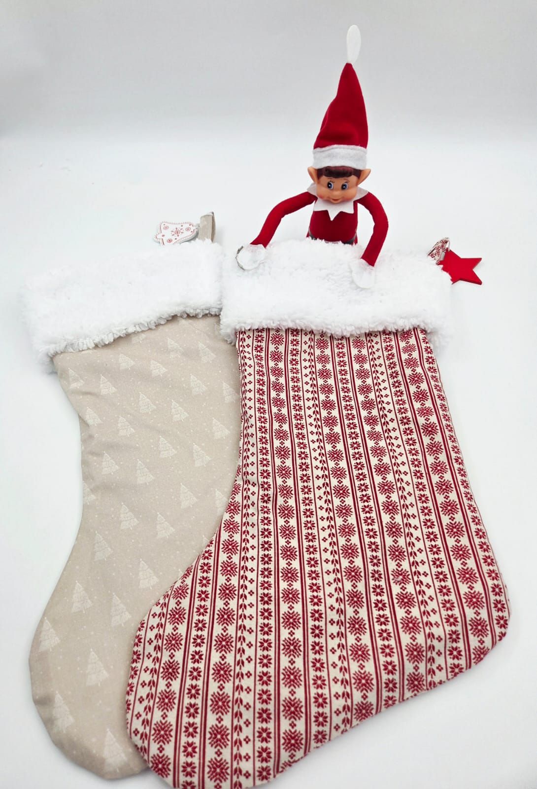 Elf on the Shelf doll sitting in a red Nordic-patterned Christmas stocking beside a beige tree-print stocking.