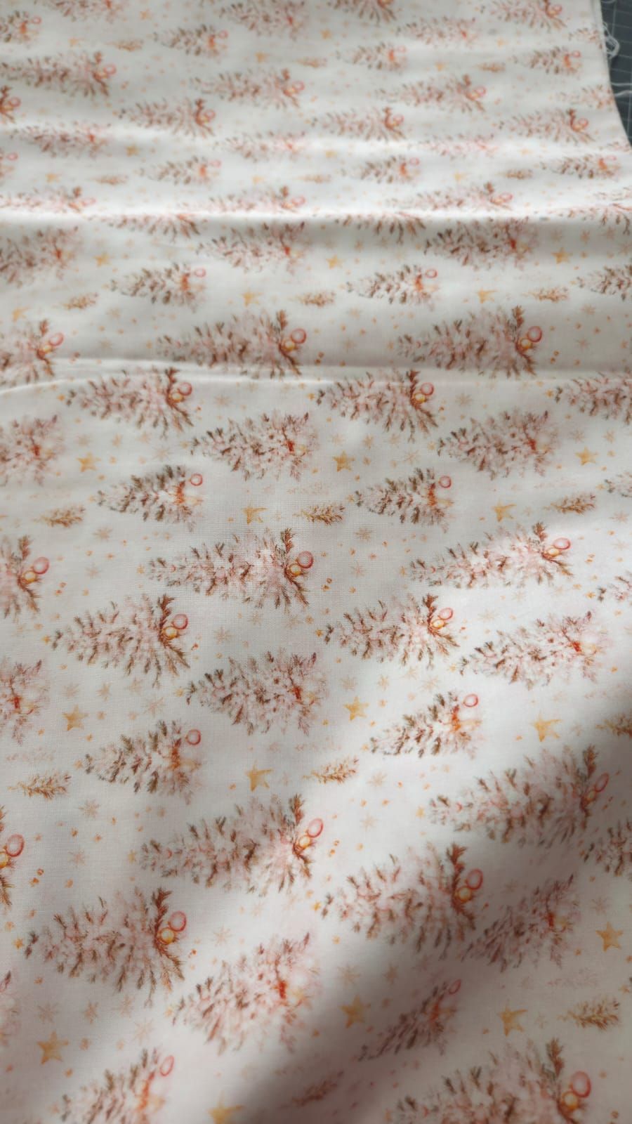 White fabric with a repeating pattern of delicate pink and gold Christmas trees and stars, perfect for holiday sewing projects.