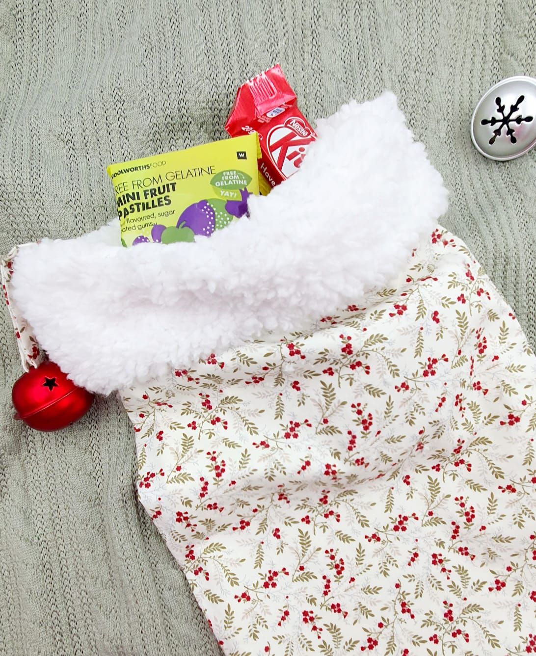A festive Christmas stocking with white faux fur trim and holly berry print fabric, filled with holiday candy and treats.
