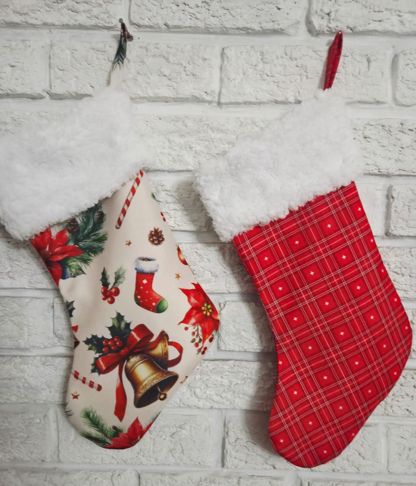 Two festive Christmas stockings with white fur trim hang on a brick wall, one with holiday prints and one red plaid.