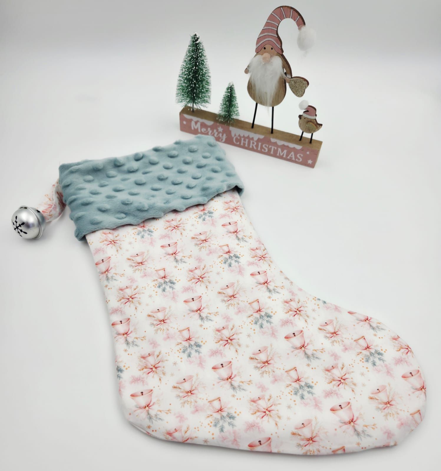 A quilted Christmas stocking with pink floral print and teal minky cuff, displayed near a holiday gnome decoration.