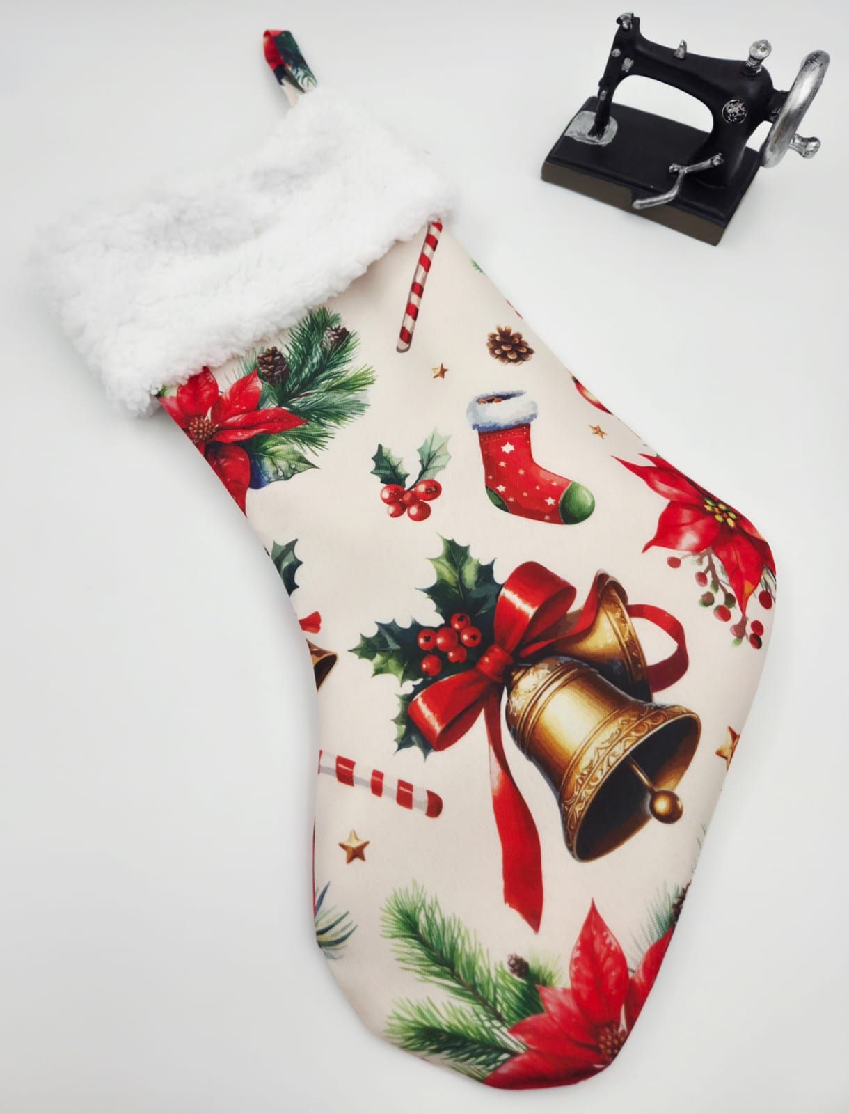 Festive Christmas stocking with white fur trim, featuring holiday bells, poinsettias, holly, and candy canes on cream fabric.