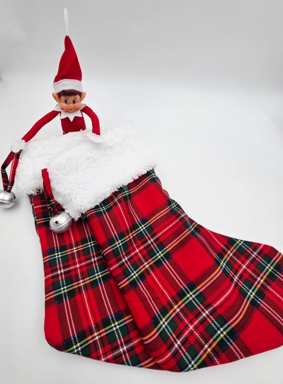 Elf on the Shelf doll peeking out of a red tartan plaid Christmas stocking with white fur trim and silver bells.
