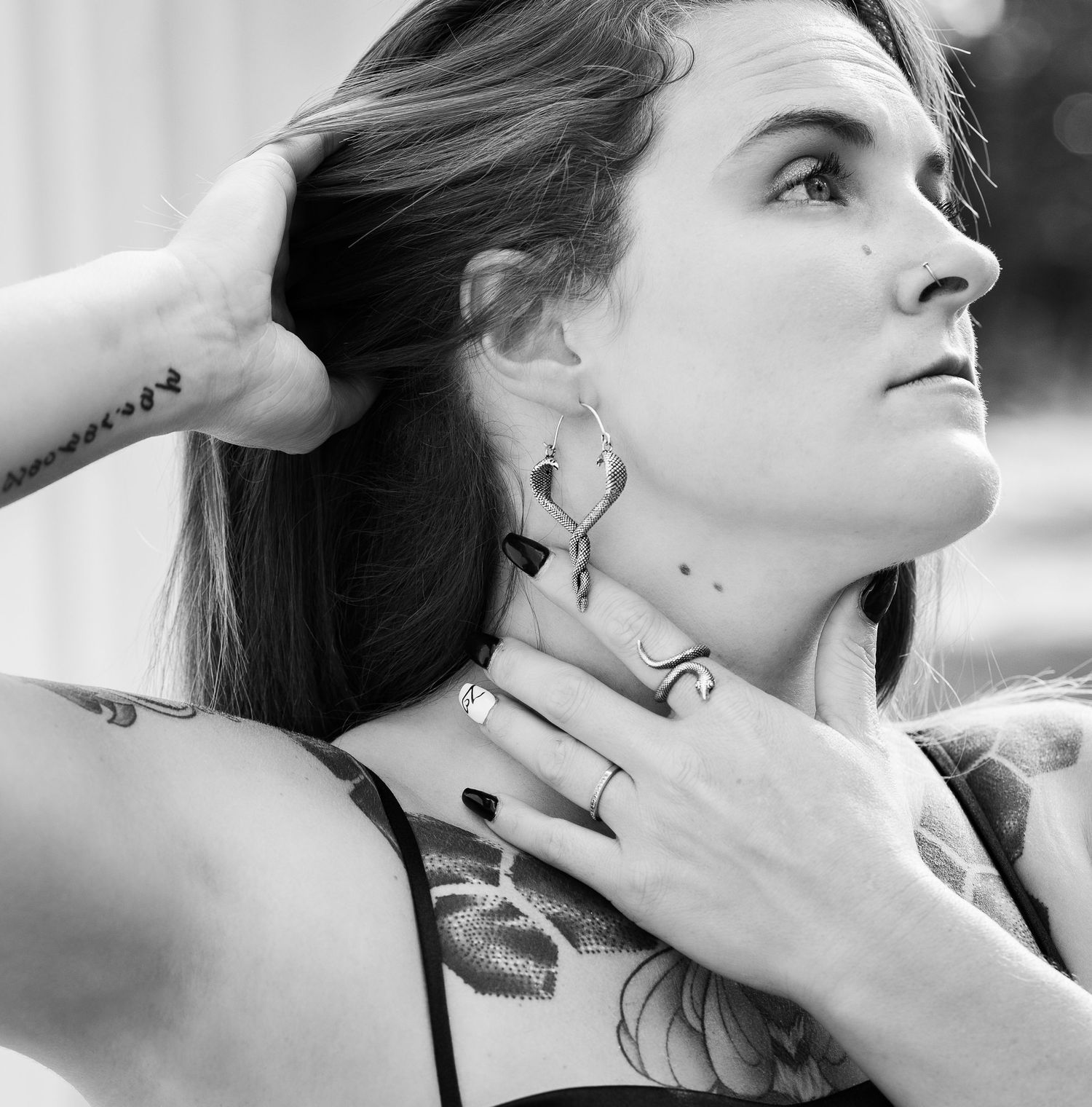 Artistic black and white portrait showing neck tattoos and jewelry details.