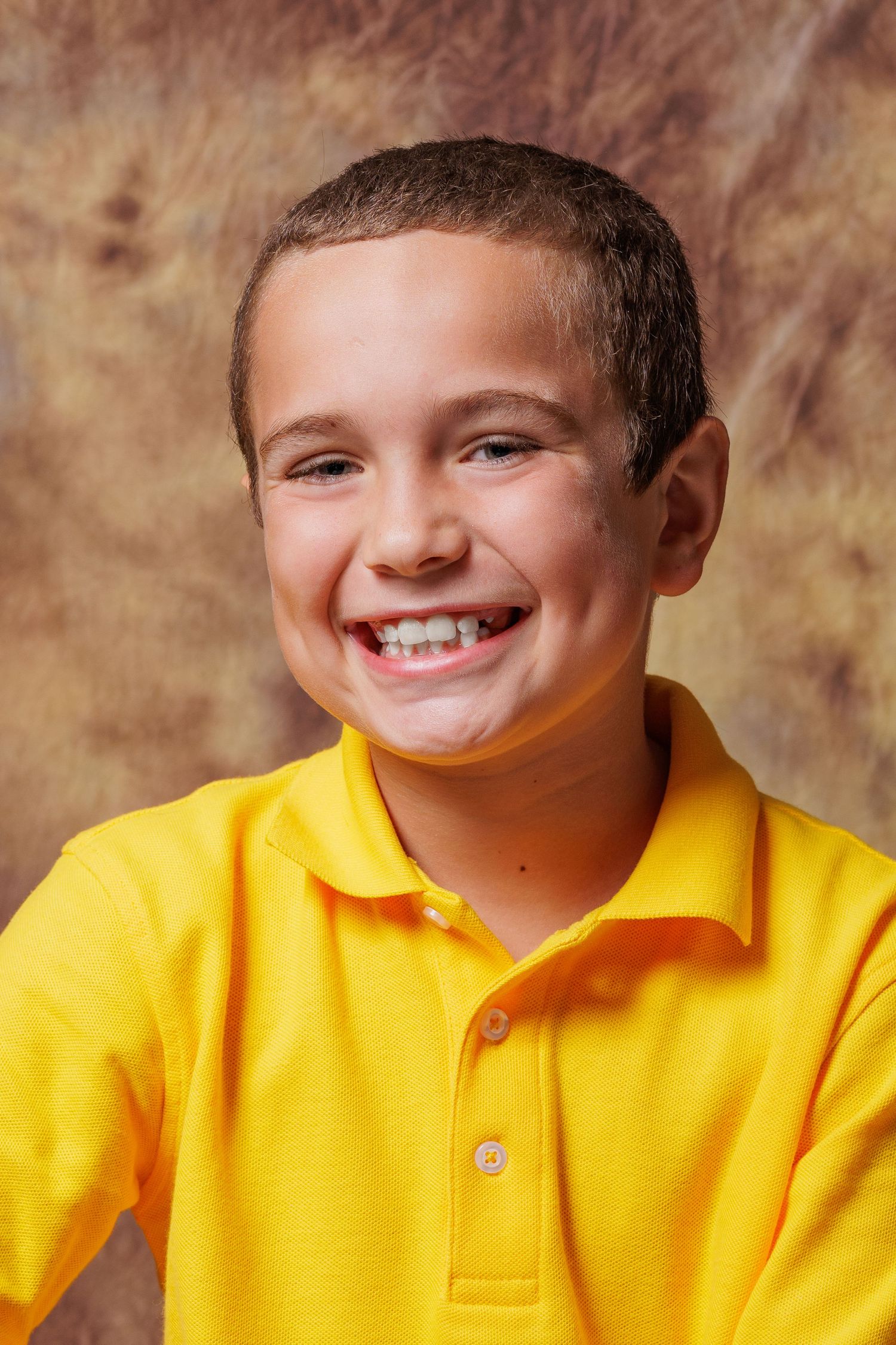 Studio portrait of someone in bright yellow polo shirt against brown background.
