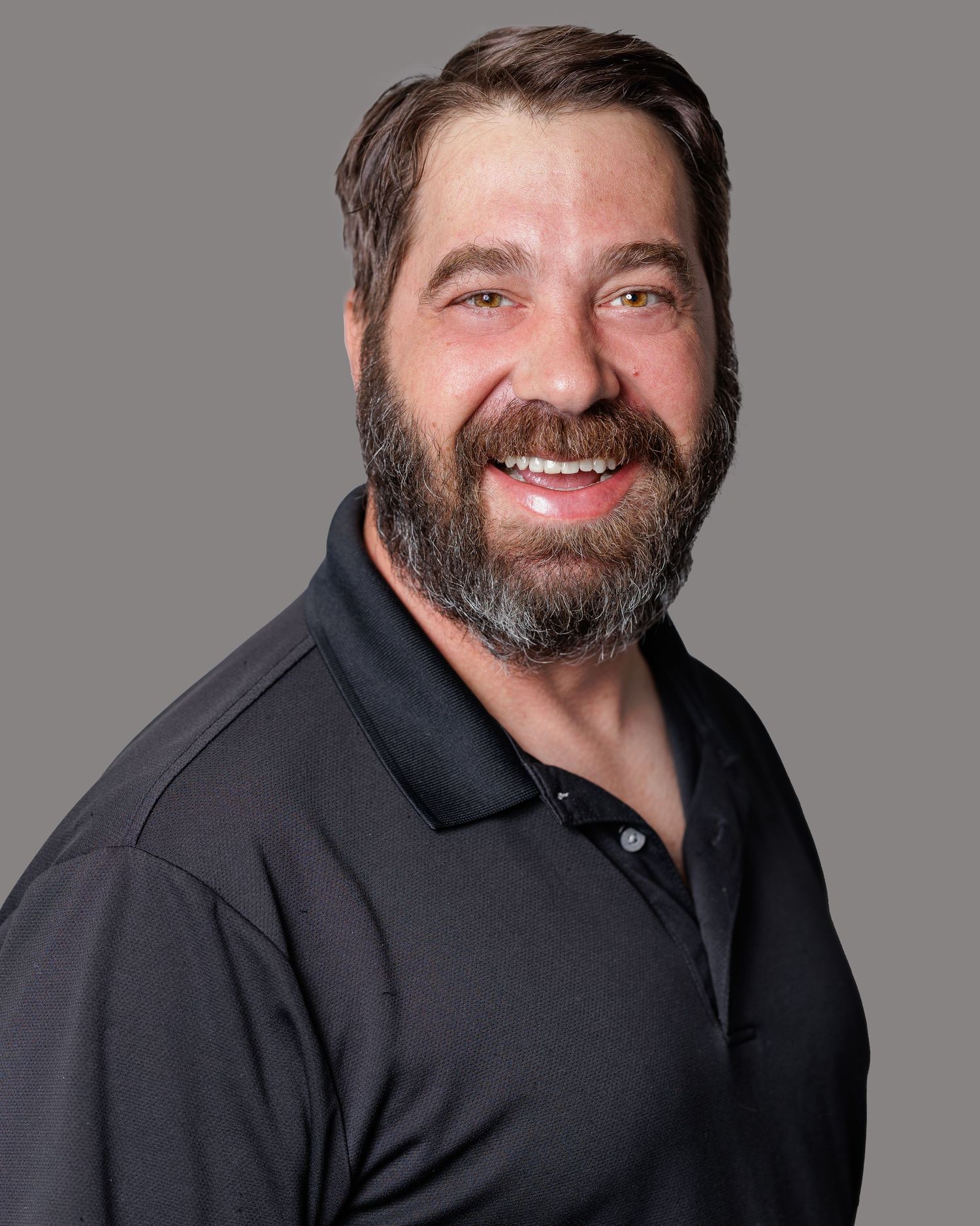 Professional headshots of a person in a black polo shirt with a beard against a gray background.