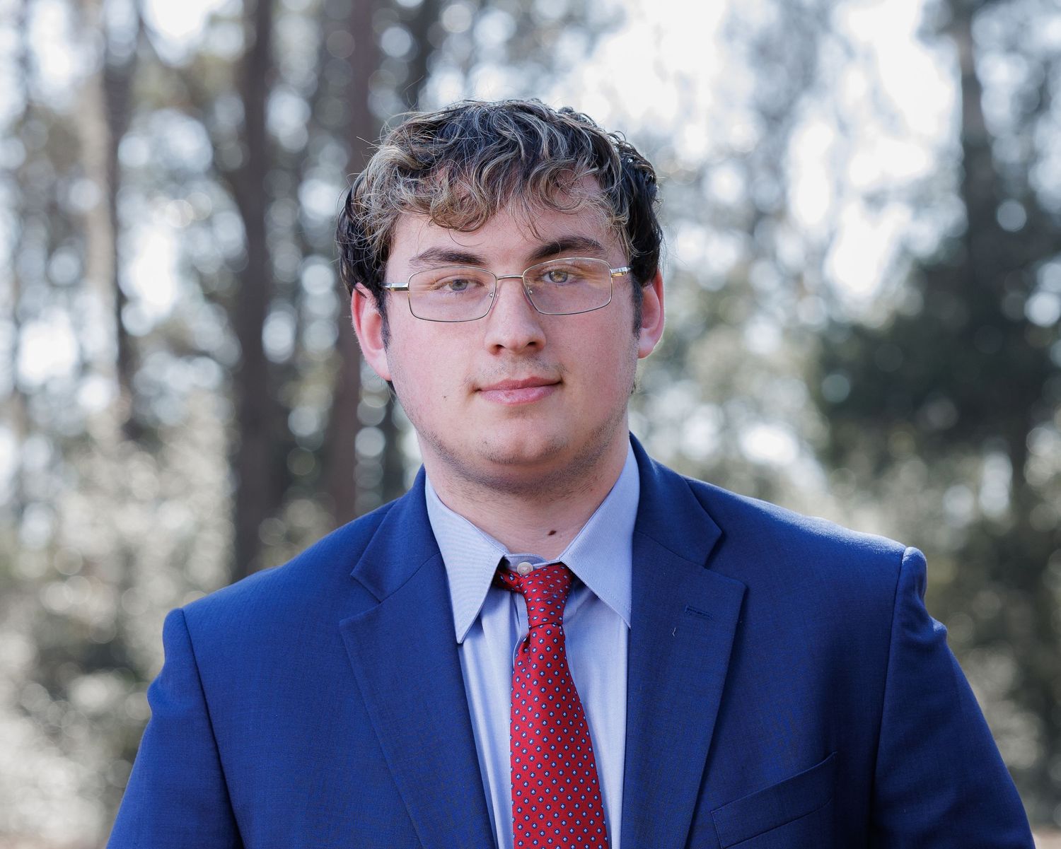 A person in a navy blue suit and red tie poses for a series of professional headshots.