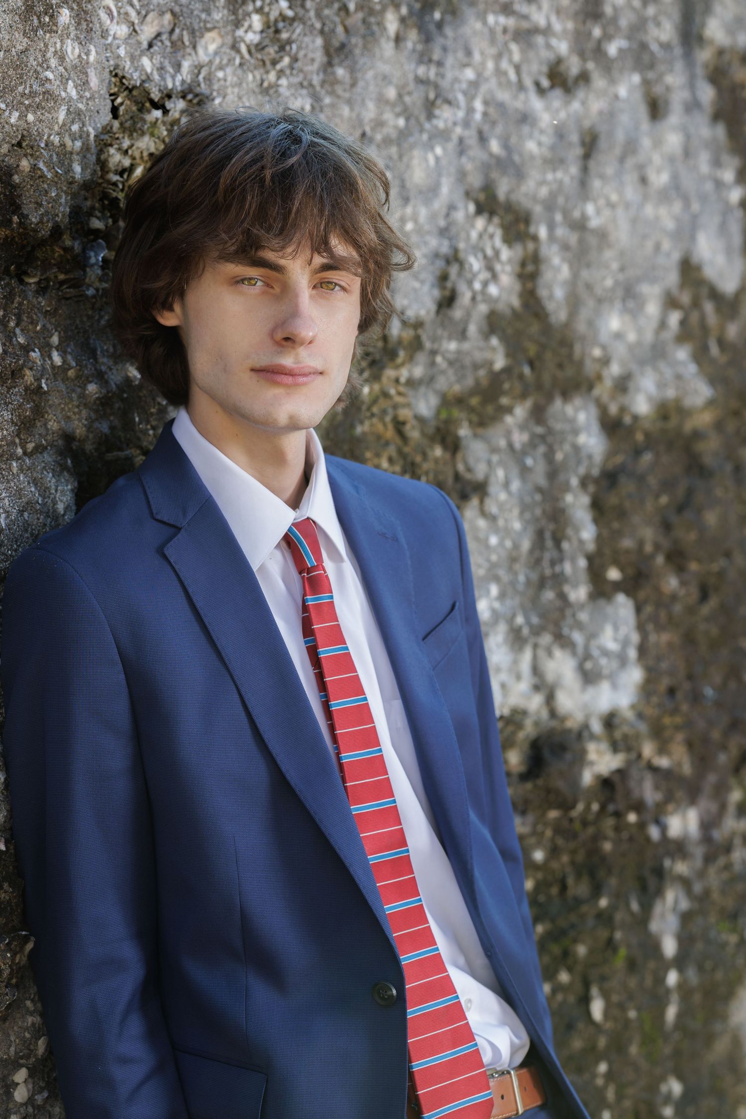 Professional portraits of someone in formal attire against a textured stone wall background.