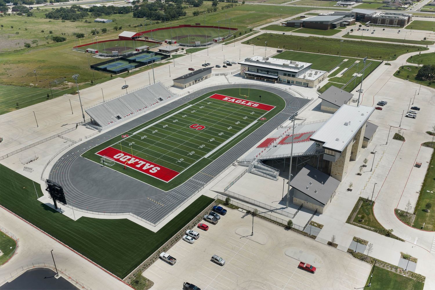 Aerial view of a high school football stadium with red turf and surrounding facilities.