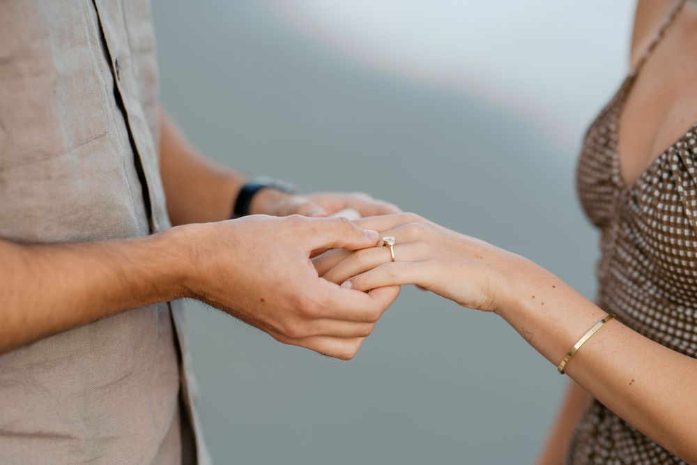Close-up of a couple holding hands, woman wearing a diamond engagement ring and gold bracelet.