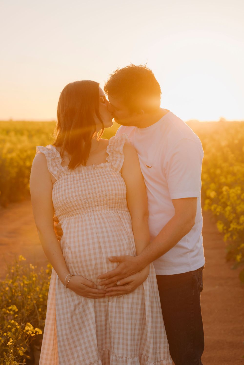 Couple sharing tender kiss in golden sunset light in blooming yellow field.