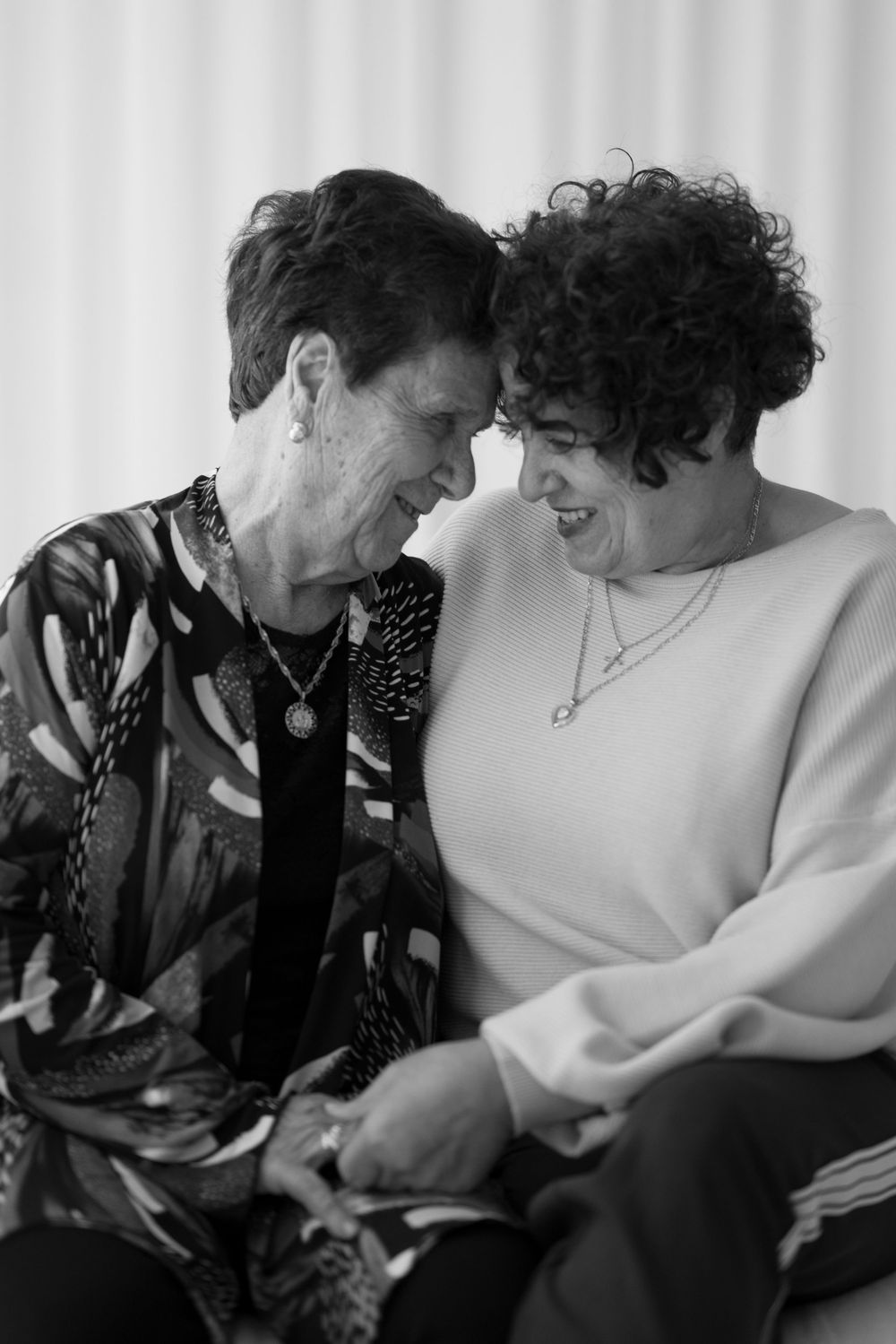 Black and white portrait of two older women laughing together with heads touching.
