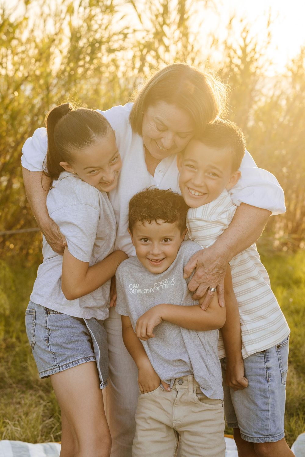 Happy mother hugging three children outdoors in golden sunset light.