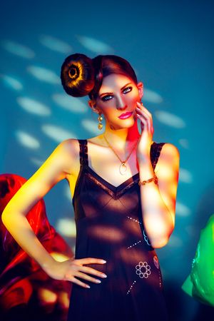 Elegant woman in black dress with updo hairstyle posing under colorful studio lighting.