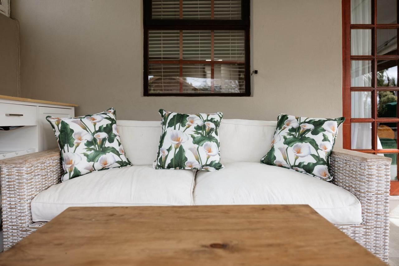 White wicker outdoor sofa with floral green and pink cushions on a covered patio with wooden coffee table.
