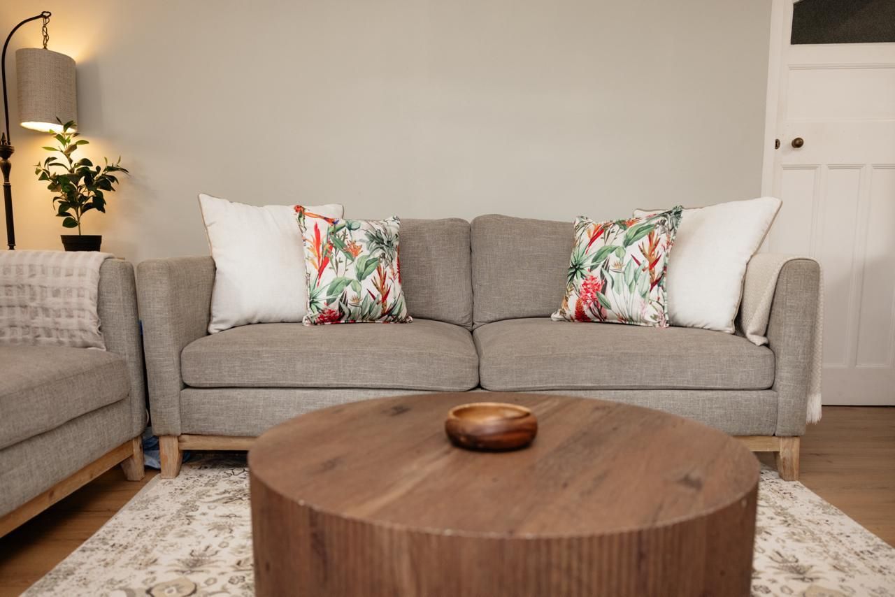Gray sofa with tropical and white throw pillows beside a round wooden coffee table in a modern living room.