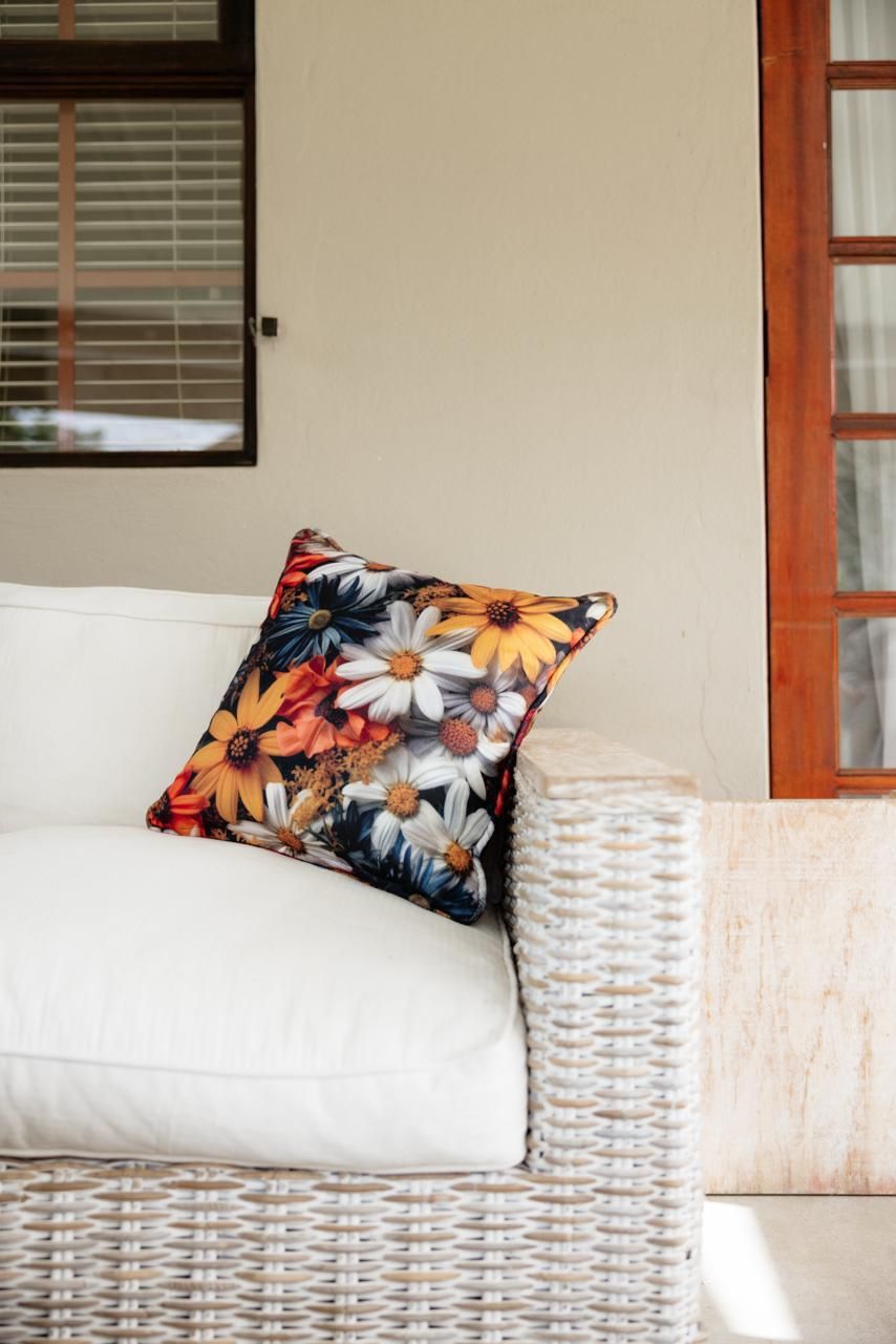 Wicker outdoor sofa with white cushions and a colorful floral throw pillow on a patio.