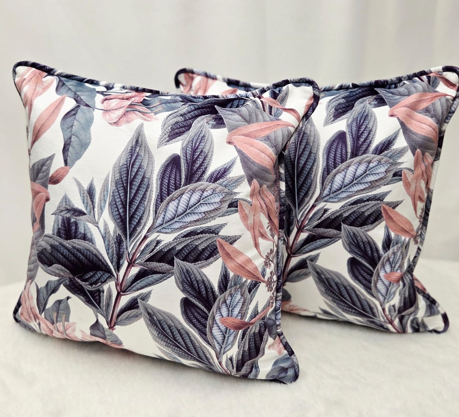 Set of two decorative throw pillows with navy blue and pink tropical leaf print pattern on white background.