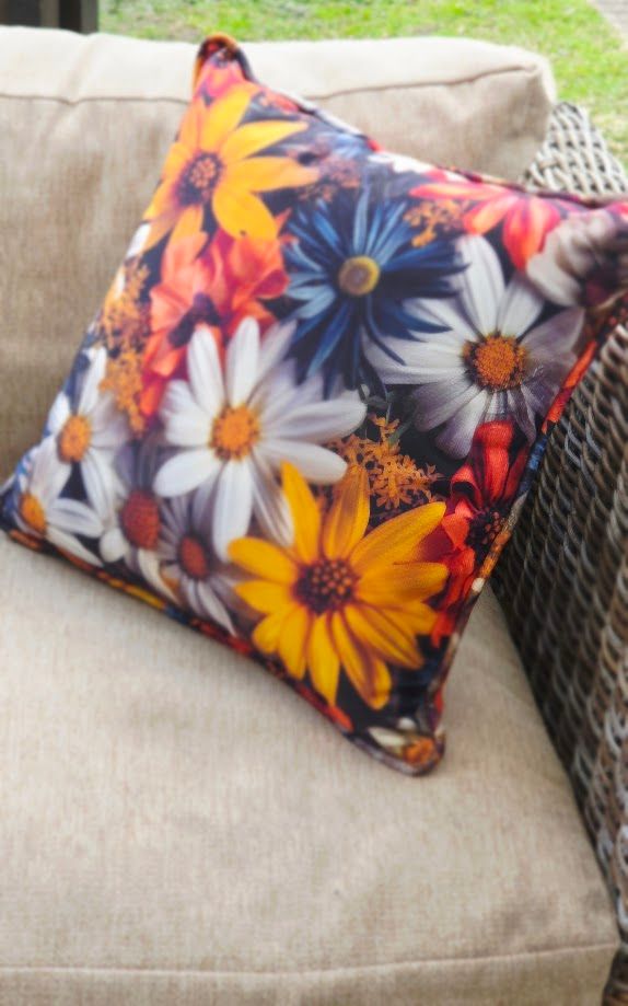 Vibrant floral throw pillow with colorful daisies in yellow, white, blue, and red on a beige outdoor sofa.