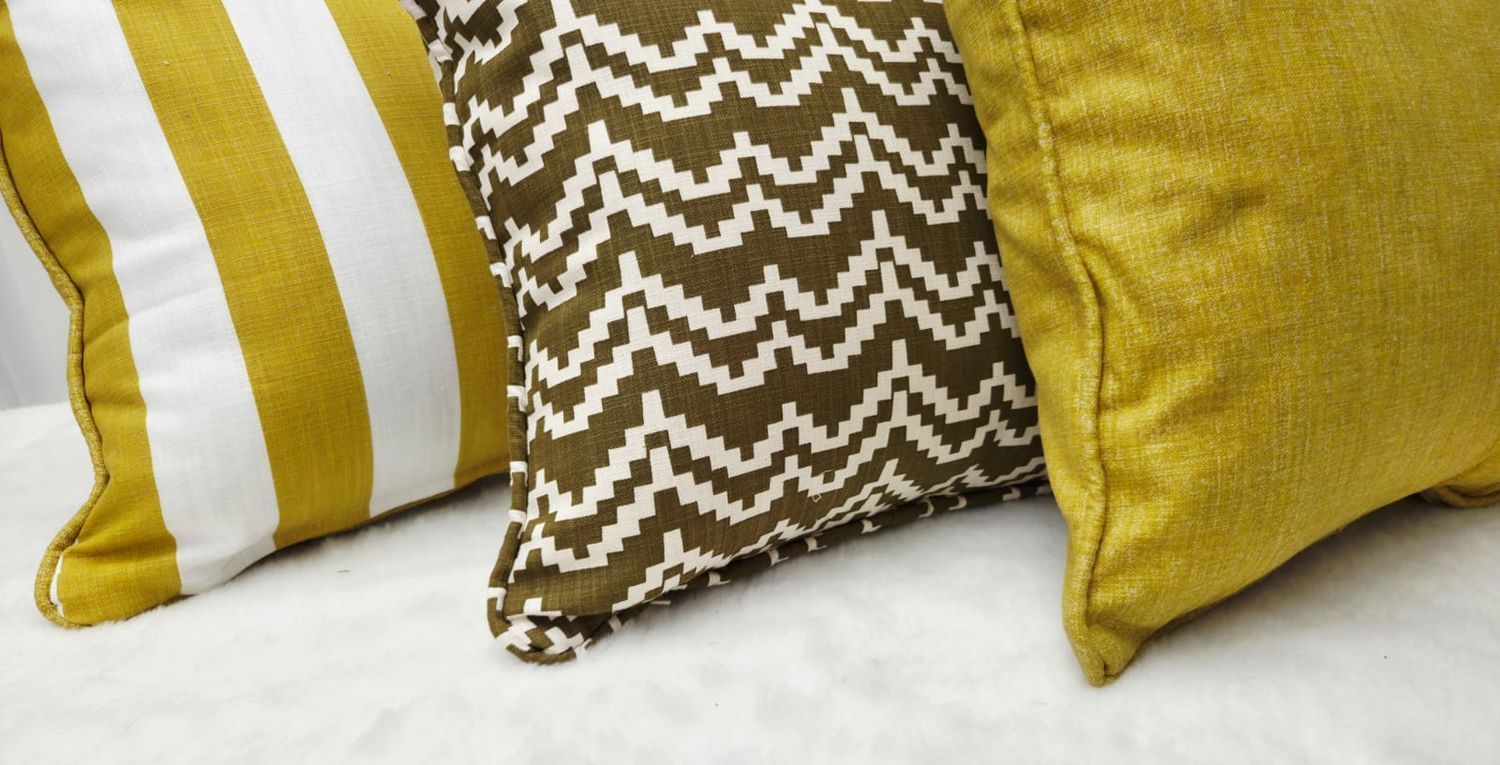 Three decorative throw pillows in gold and brown tones featuring stripe, chevron, and solid linen patterns on a white surface.